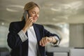 Female sales manager looking at wristwatch to checking time while having a phone call with client Royalty Free Stock Photo