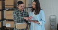 A female sales manager using a tablet computer is talking to a male worker holding a cardboard package. A warehouse with Royalty Free Stock Photo