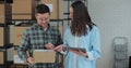 A female sales manager using a tablet computer is talking to a male worker holding a cardboard package. A warehouse with Royalty Free Stock Photo