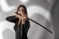 A female samurai in black clothing with long dark hair swung a katana from behind her left shoulder, against a gray background wit