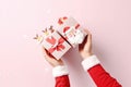 Female, Santa hands in pastel pullover holding gift box with Christmas design on light pastel background