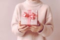 Female, Santa hands in pastel pullover holding gift box with Christmas design on light pastel background