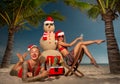 Female Santas relaxing on the beach with sandman, champagne and fruits on a tropical sandy beach with palm trees Royalty Free Stock Photo