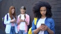 Female school pupils scrolling smartphones outdoors, gadget addiction, internet