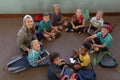 Female school teacher sitting cross legged on the floor in a circle with a group of schoolchildren i Royalty Free Stock Photo