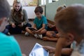 Female school teacher sitting cross legged on the floor in a circle with a group of schoolchildren a Royalty Free Stock Photo