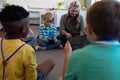 Female school teacher sitting cross legged on the floor in a circle with a group of schoolchildren Royalty Free Stock Photo