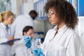 Female Scientific Researcher In Laboratory, African American Woman Working With Flask Over Group Of Scientist Making Royalty Free Stock Photo