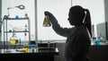 A Female Scientist Holds An Erlenmeyer Flask With A Plant Inside And Examines It. Dark Silhouette Of A Scientist With A