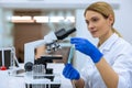 Female scientist using microscope, holding test tube, analyzing liquid biochemicals in laboratory.