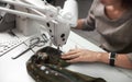 Seamstress working on modern electrical sewing machine making exclusive garments in fashion studio.