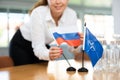 Female secretary places flags of the NATO (OTAN) and Russia on the table before negotiations of top political