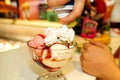 Female Seller pours sauce on ice cream. Woman hard making ice cream copper cup with forest fruit and candy.