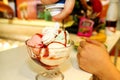 Female Seller pours sauce on ice cream. Woman hard making ice cream copper cup with forest fruit and candy.