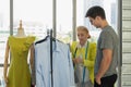 Female senior dressmaker offer her design clothing to young male customer at dressmaker shop and fashion design studio
