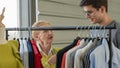 Female senior dressmaker offer her design clothing to young male customer at dressmaker shop and fashion design studio