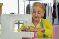 Female senior dressmaker using sewing machine making dress at fashion design shop