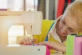 Female senior dressmaker using sewing machine making dress at fashion design shop