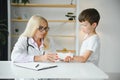 Female senior pediatrician showing x-ray of wrist and hand to little boy patient. Child at doctors office