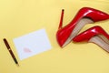 female shiny red stilettos and a card with a lipstick print on a yellow background
