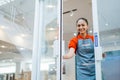 female shop assistant in apron smiling while opening the glass door