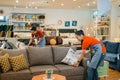 female shop assistant in apron tidying up sofa cushions at furniture store