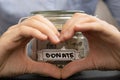 Female showing heart sign with hands Saving Money In Glass Jar filled with Dollars banknotes. DONATE transcription in Royalty Free Stock Photo