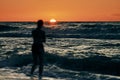 Female silhouette in blue sea waves at summer sunset, half sun below horizon, beachfront holiday