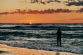Female silhouette in blue sea waves at summer sunset, half sun below horizon, beachfront holiday