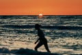 Female silhouette walking in sea waves at summer sunset, half sun below horizon, beachfront holiday