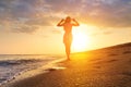 Female silhouette, rear view, with hands raised to the hat and hair flowing. Seascape during golden sunrise with