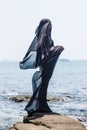 Female silhouette wrapped in black fabric posing at the rocky seaside Royalty Free Stock Photo