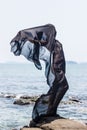 Female silhouette wrapped in black fabric posing at the rocky seaside Royalty Free Stock Photo