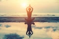 Female silhouette in yoga with reflection in water, meditation pose at sunset.