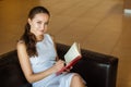 Female sitting on black sofa in white luxury dress and taking notes Royalty Free Stock Photo