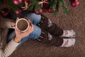 Female sitting on floor and warmers leg socket and with cup of coffee in hand and next to Christmas tree Royalty Free Stock Photo