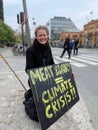 Female sitting on an urban sidewalk, holding an Extinction Rebellion protest sign in her hands