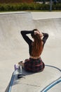 Female skater sitting on a ramp top with a glass bottle of water. Cool young roller blader chilling in a skatepark in a sunny