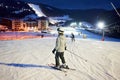 Female skier after skiing day standing on skis. Ski resort lighted by lanterns and mountain in darkness on background. Royalty Free Stock Photo