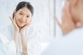 Female Skin Care. Young asian woman touching her face and looking to mirror in bathroom. Royalty Free Stock Photo