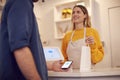 Female Small Business Owner Accepting Contactless Payment In Shop From Customer Using Mobile Phone