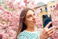 Female with smartphone taking selfie in cherry flower blossom garden. Young smiling european white caucasian woman with mobile Royalty Free Stock Photo