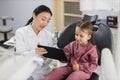 Female smiling asian dentist showing tablet pc computer to happy kid patient, Royalty Free Stock Photo