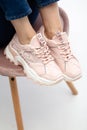 Female sneakers on legs. Pink woman`s shoes on feet on chair.