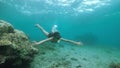 A female snorkeler swimming underwater in the deep blue ocean full of corals.