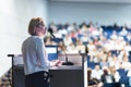 Female speaker giving a talk on corporate business conference. Unrecognizable people in audience at conference hall Royalty Free Stock Photo