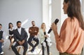 Female speaker with microphone in her hand speaks in front of small group of business people.