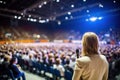 female speaker stands illuminated by a spotlight against a mysterious blurred people background, business coach