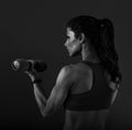 Female sporty muscular woman doing strength workout on the shoulders, biceps and arms in sport bra holding dumbbells on grey Royalty Free Stock Photo