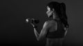 Female sporty muscular young serious woman doing strength workout on the shoulders, biceps and arms in sport bra holding dumbbells Royalty Free Stock Photo